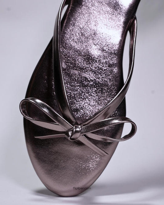 Person wearing black bow-detail sandals while standing on a stone walkway