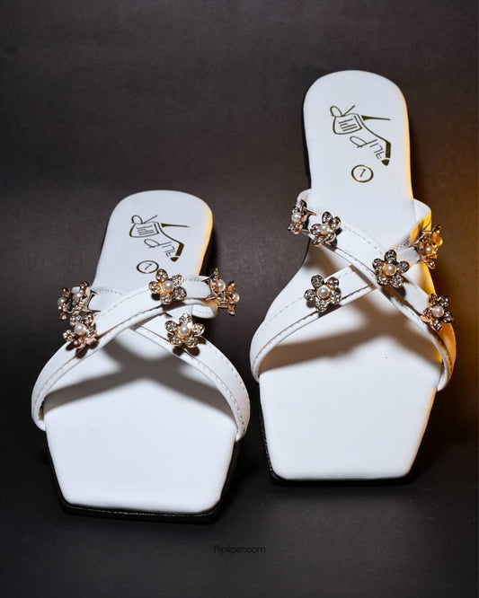 White sandals with gold floral embellishments displayed on a beige fabric background