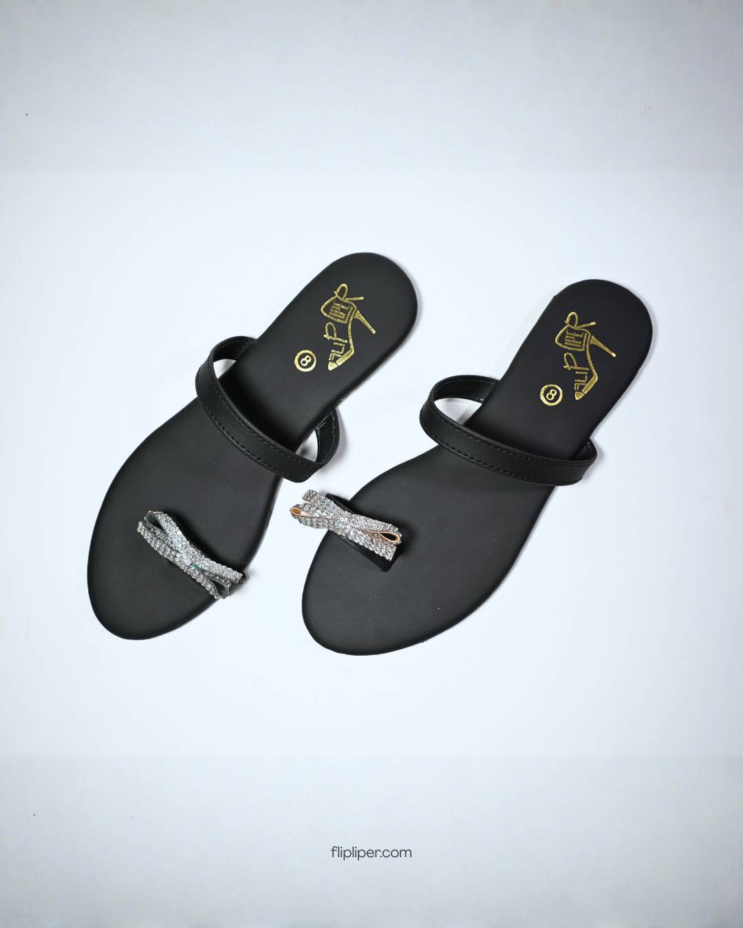Black sandals with crystal bow embellishments displayed on a b
