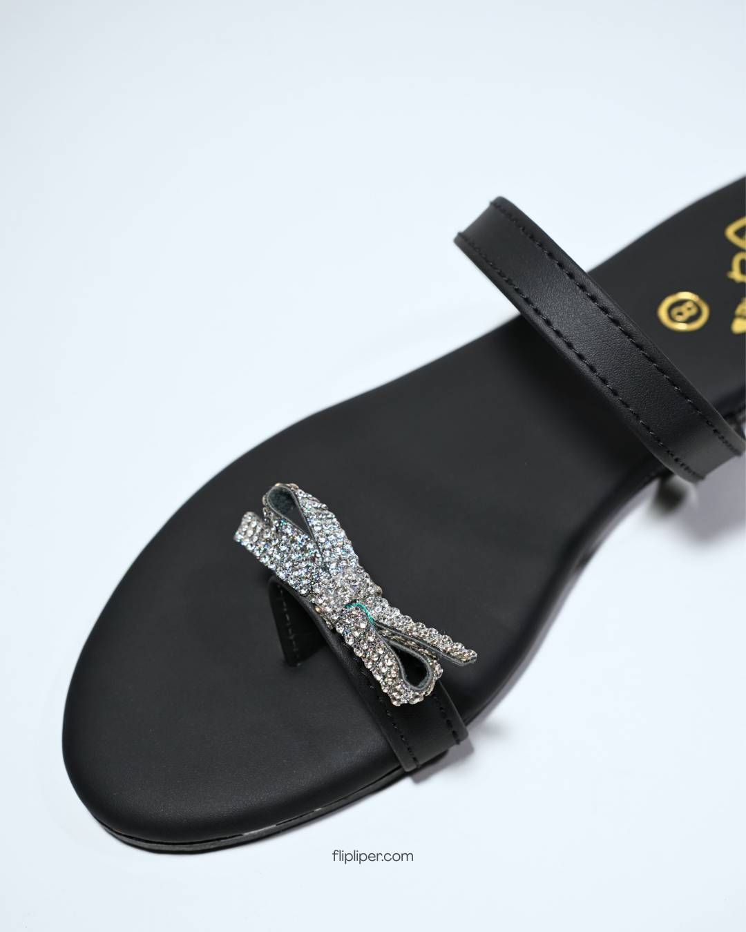 Black sandals with crystal bow embellishments displayed on a b
