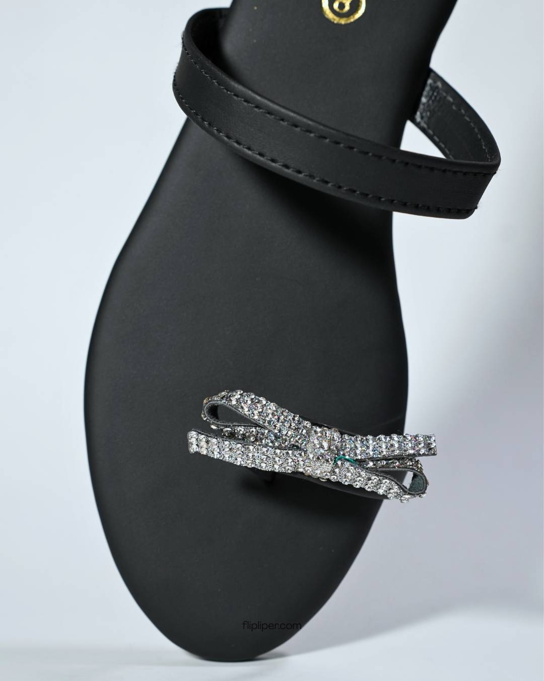 Black sandals with crystal bow embellishments displayed on a b
