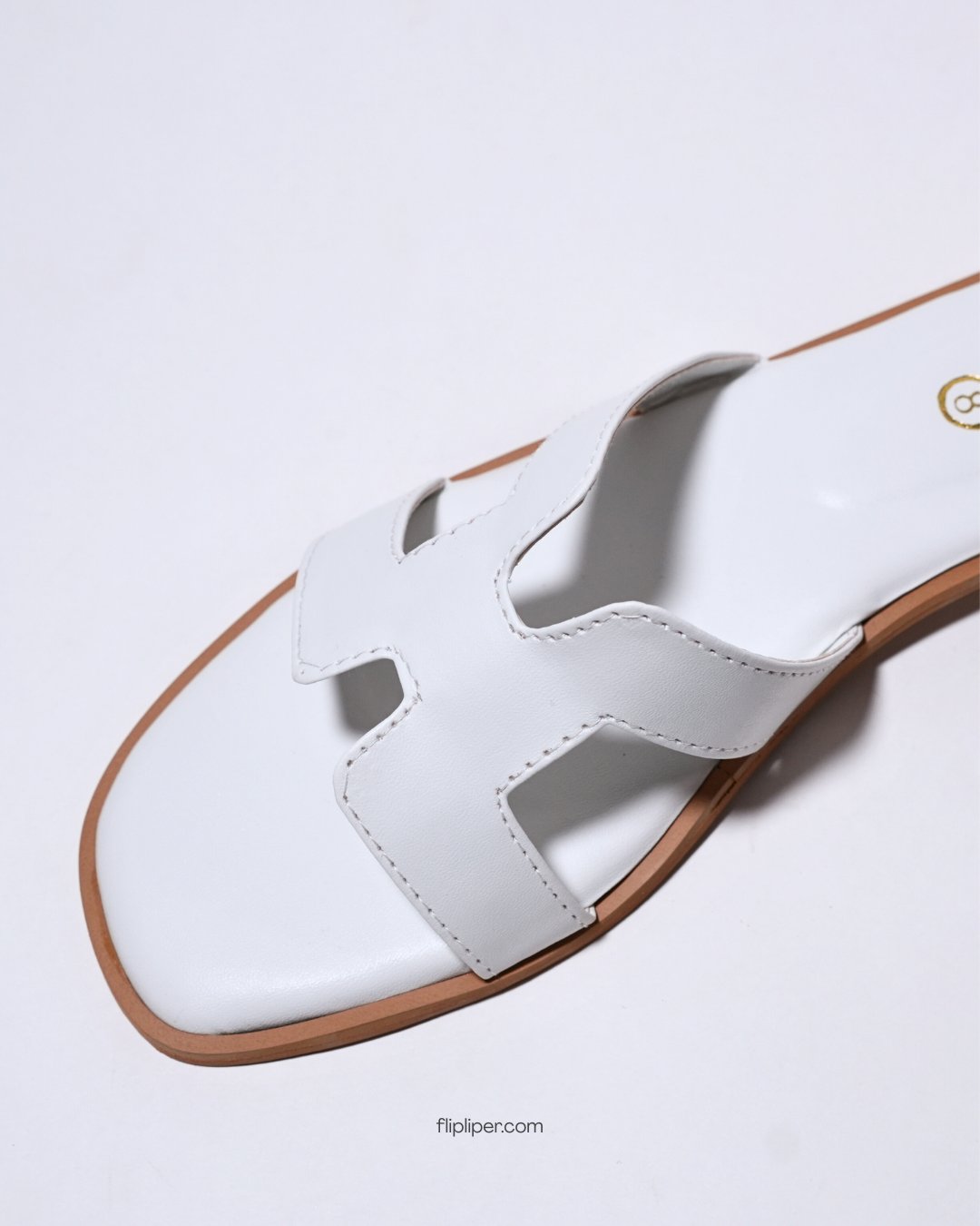 White slip-on sandals with gold detailing placed on a wooden table beside the ocean
