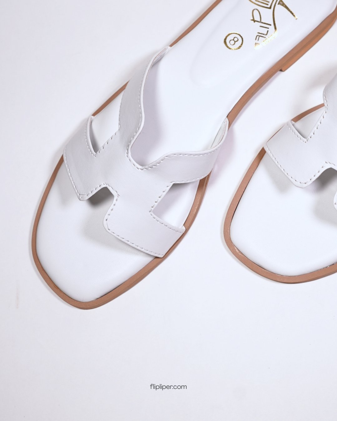 White slip-on sandals with gold detailing placed on a wooden table beside the ocean
