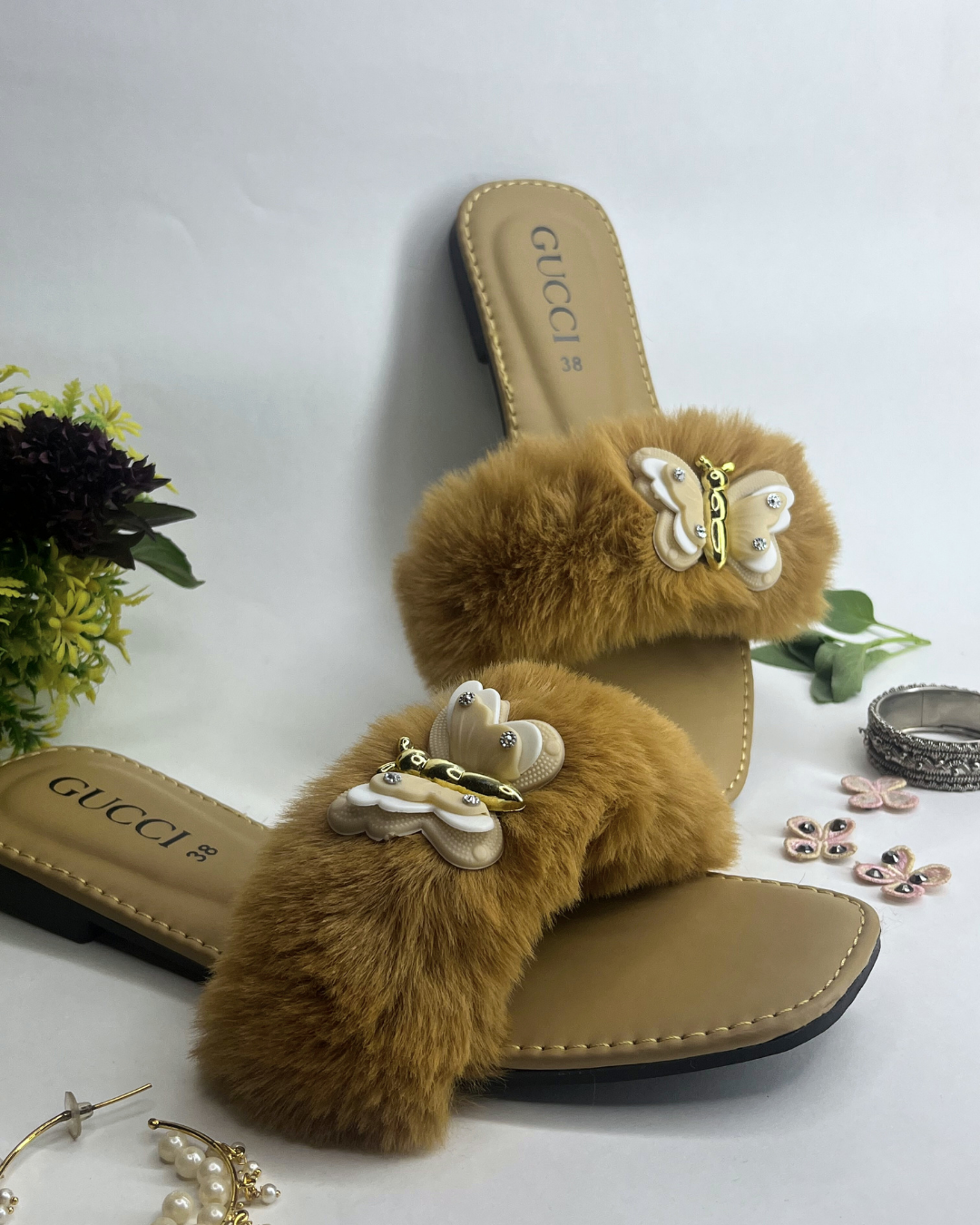 Beige women slides with fluffy fur strap and butterfly embellishment on a light background