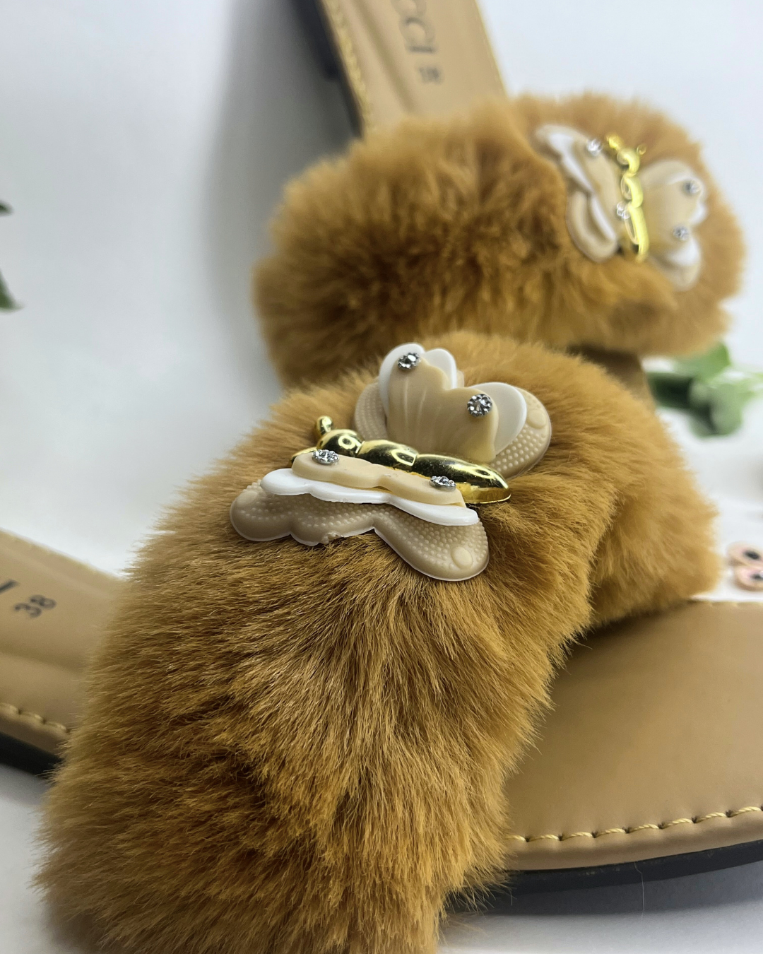 Beige women slides with fluffy fur strap and butterfly embellishment on a light background