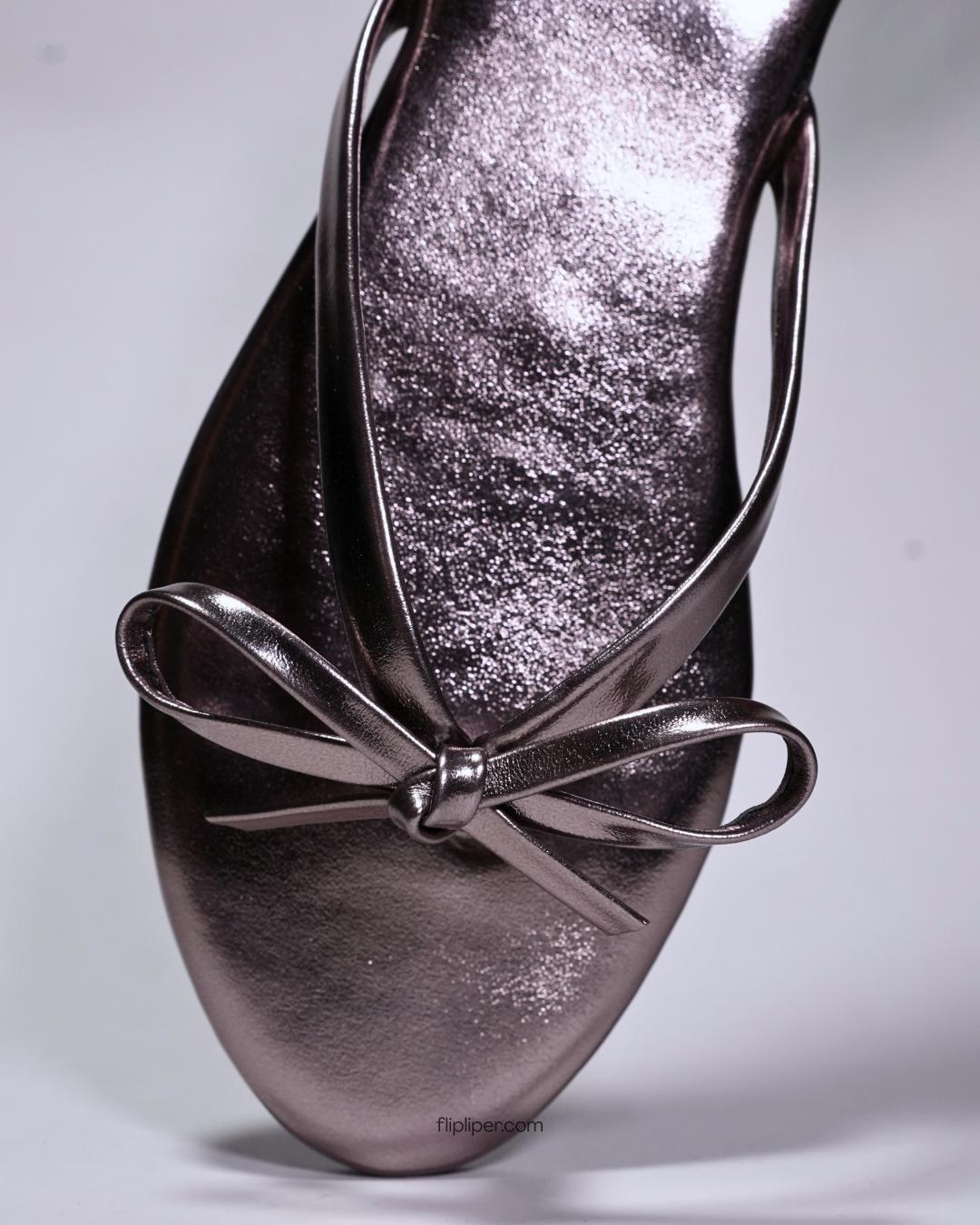 Person wearing black bow-detail sandals while standing on a stone walkway
