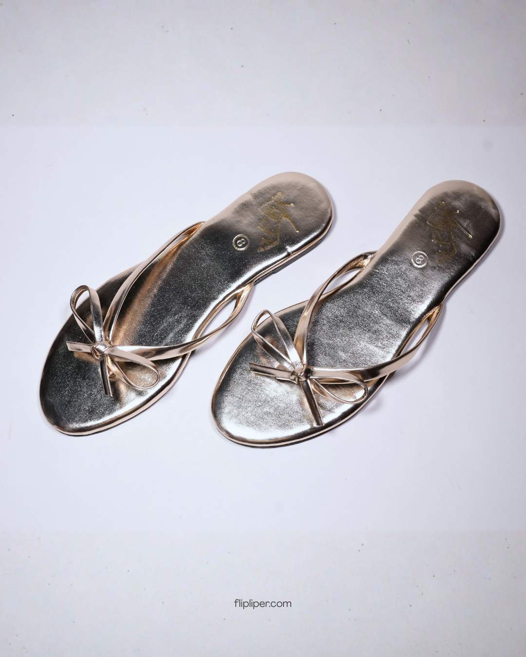 Person wearing gold bow-detail sandals while standing on a beige floor
