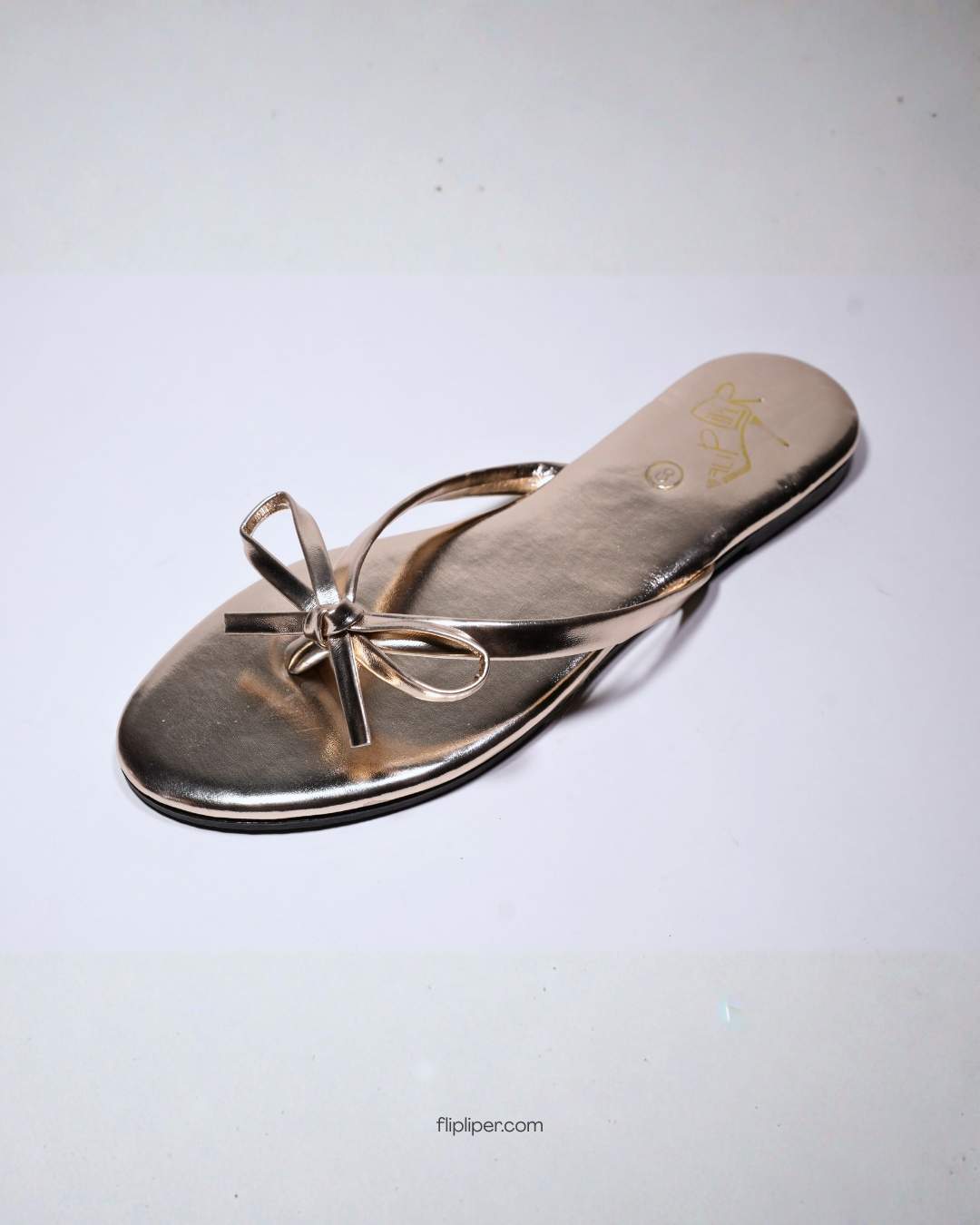 Person wearing gold bow-detail sandals while standing on a beige floor
