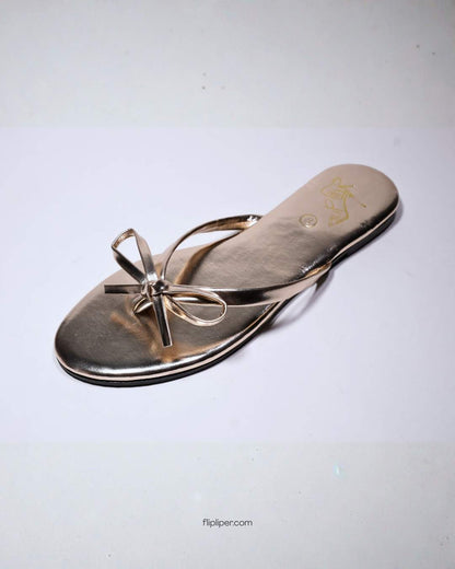 Person wearing gold bow-detail sandals while standing on a beige floor
