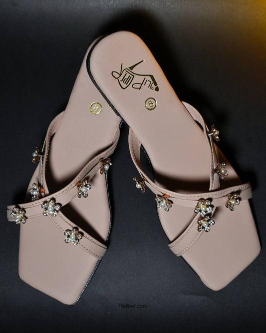 Pink sandals with decorative floral straps placed on a beige fabric background
