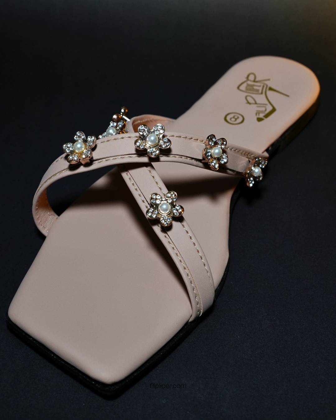 Pink sandals with decorative floral straps placed on a beige fabric background
