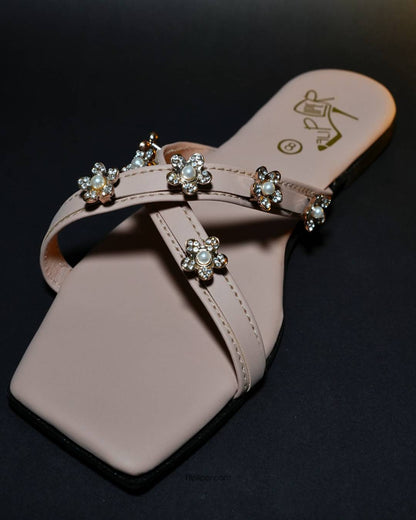 Pink sandals with decorative floral straps placed on a beige fabric background
