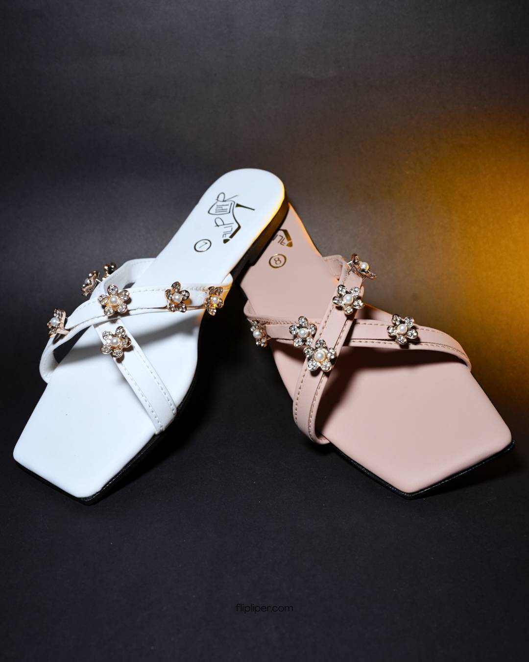 Pink sandals with decorative floral straps placed on a beige fabric background
