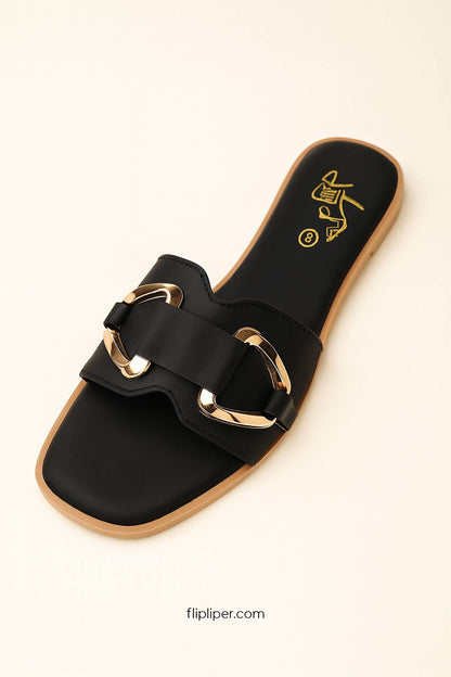 Pair of black sandals with gold buckles displayed on a beige background
