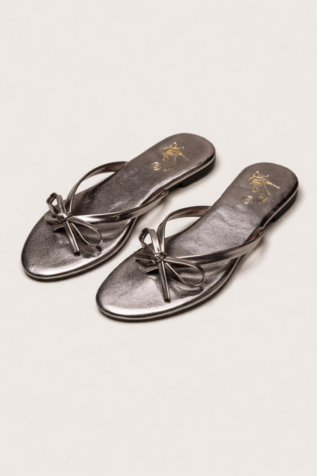 Person wearing black bow-detail sandals while standing on a stone walkway
