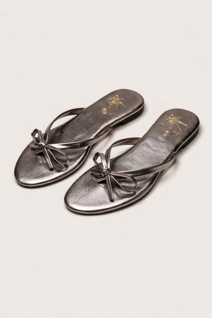 Person wearing black bow-detail sandals while standing on a stone walkway
