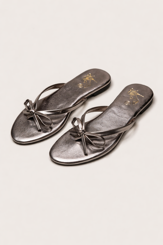 Person wearing black bow-detail sandals while standing on a stone walkway
