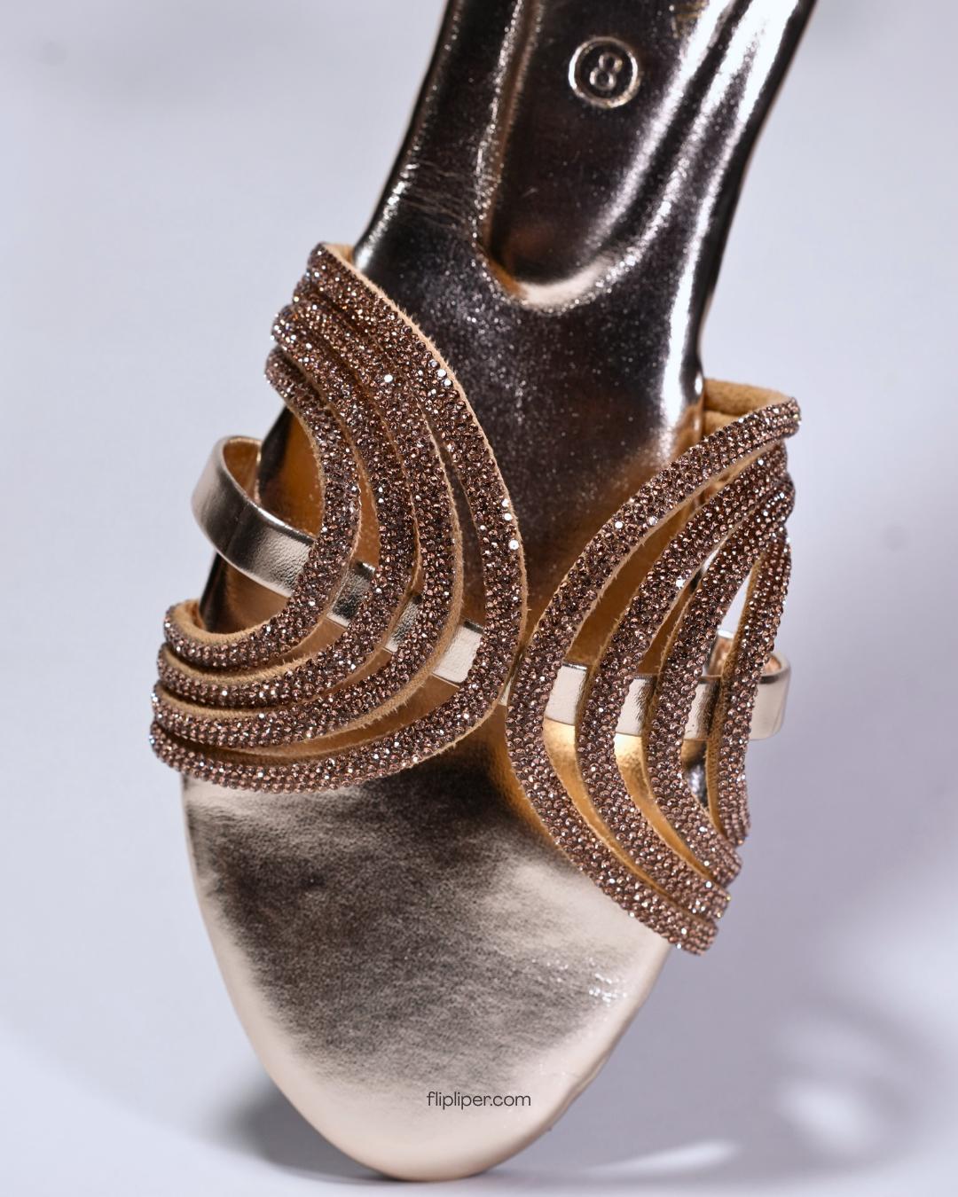 Person wearing gold embellished sandals while standing on a tiled floor
