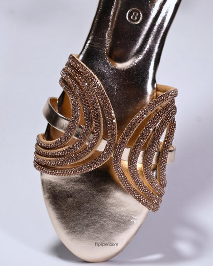 Person wearing gold embellished sandals while standing on a tiled floor
