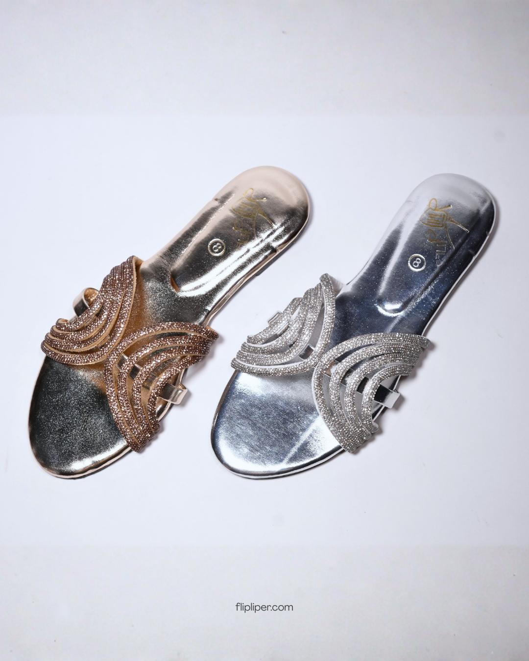 Person wearing gold embellished sandals while standing on a tiled floor
