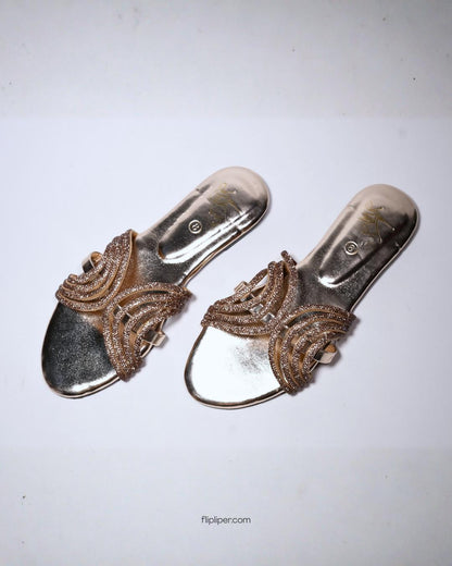 Person wearing gold embellished sandals while standing on a tiled floor
