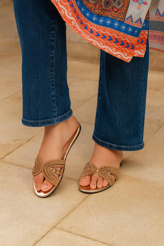 Person wearing gold embellished sandals while standing on a tiled floor
