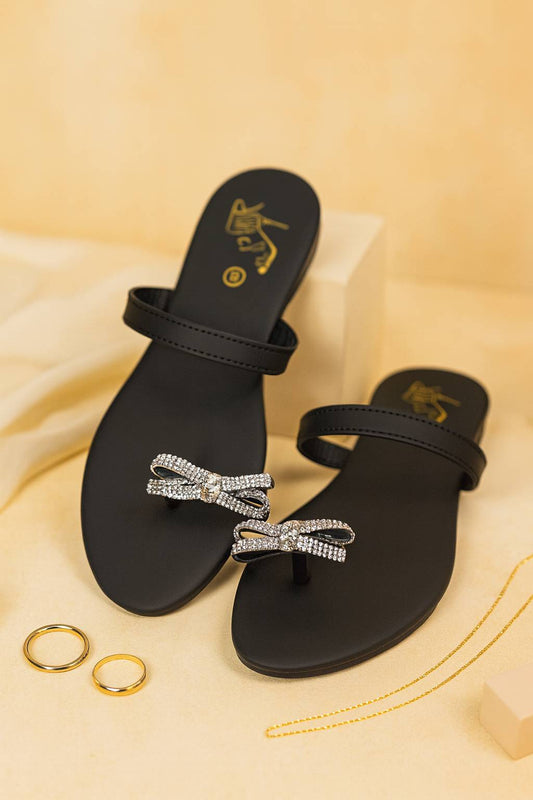 Black sandals with crystal bow embellishments displayed on a b
