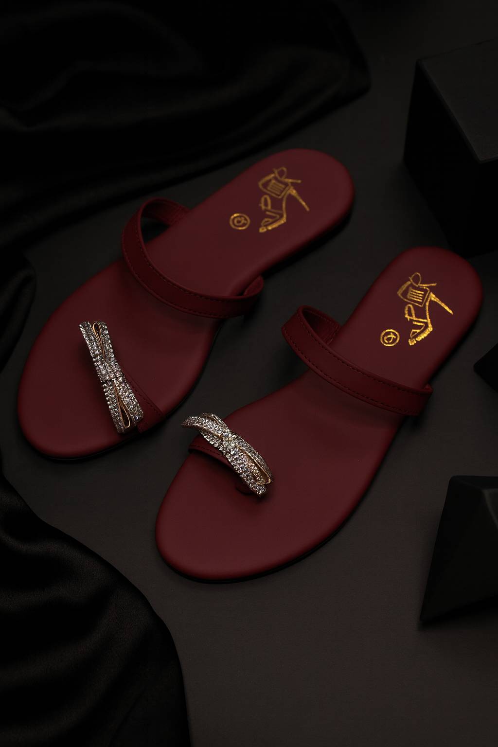 Red sandals with crystal embellishments displayed on a dark black background

