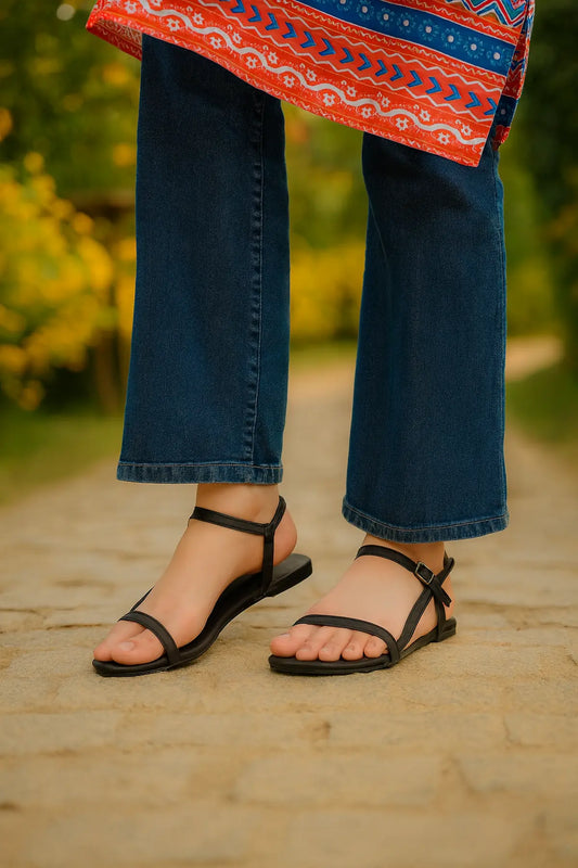 Flip Liper black flat sandals worn with blue jeans while standing on a stone pathway in an outdoor natural setting
