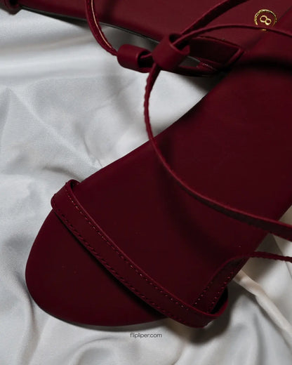 Flip Liper maroon flat sandals worn with blue jeans while walking on a stone pathway in a natural outdoor setting
