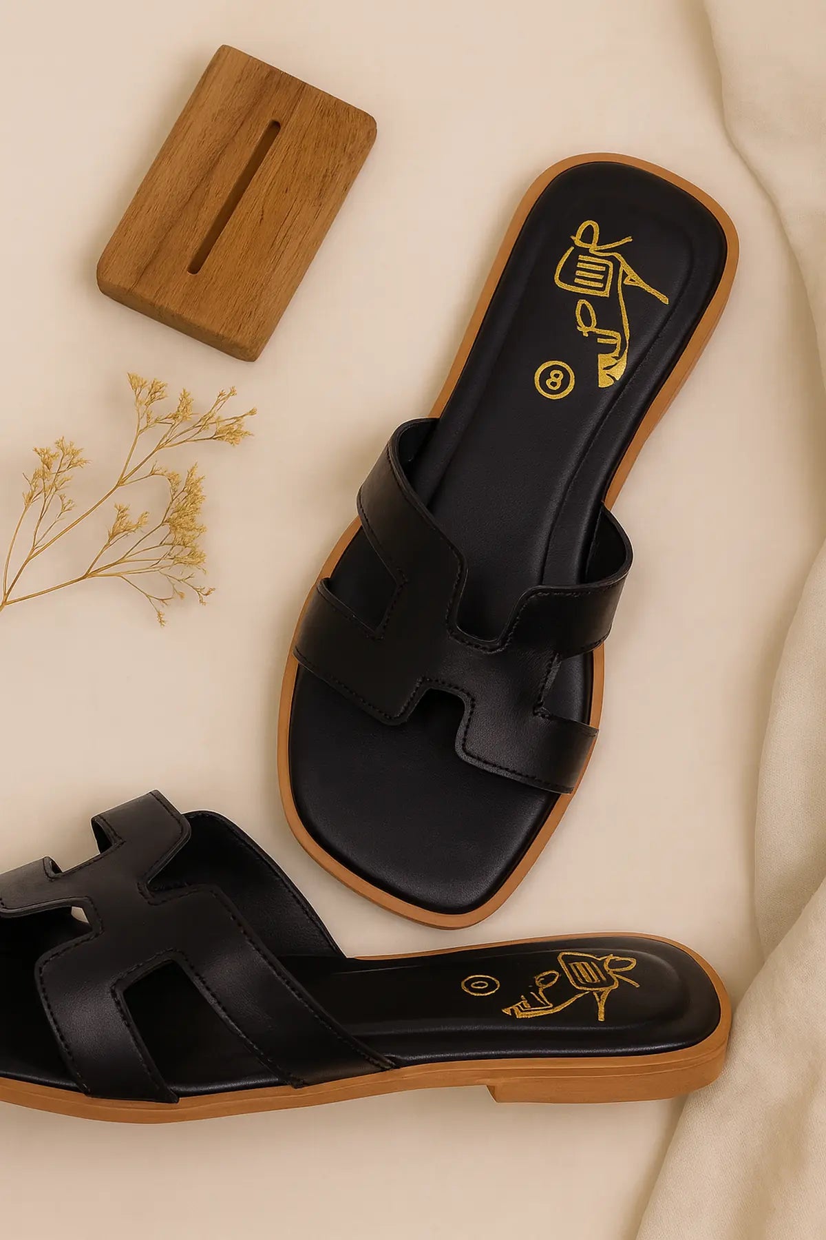 Black slip-on sandals with tan wooden soles displayed on a light beige background with minimal props
