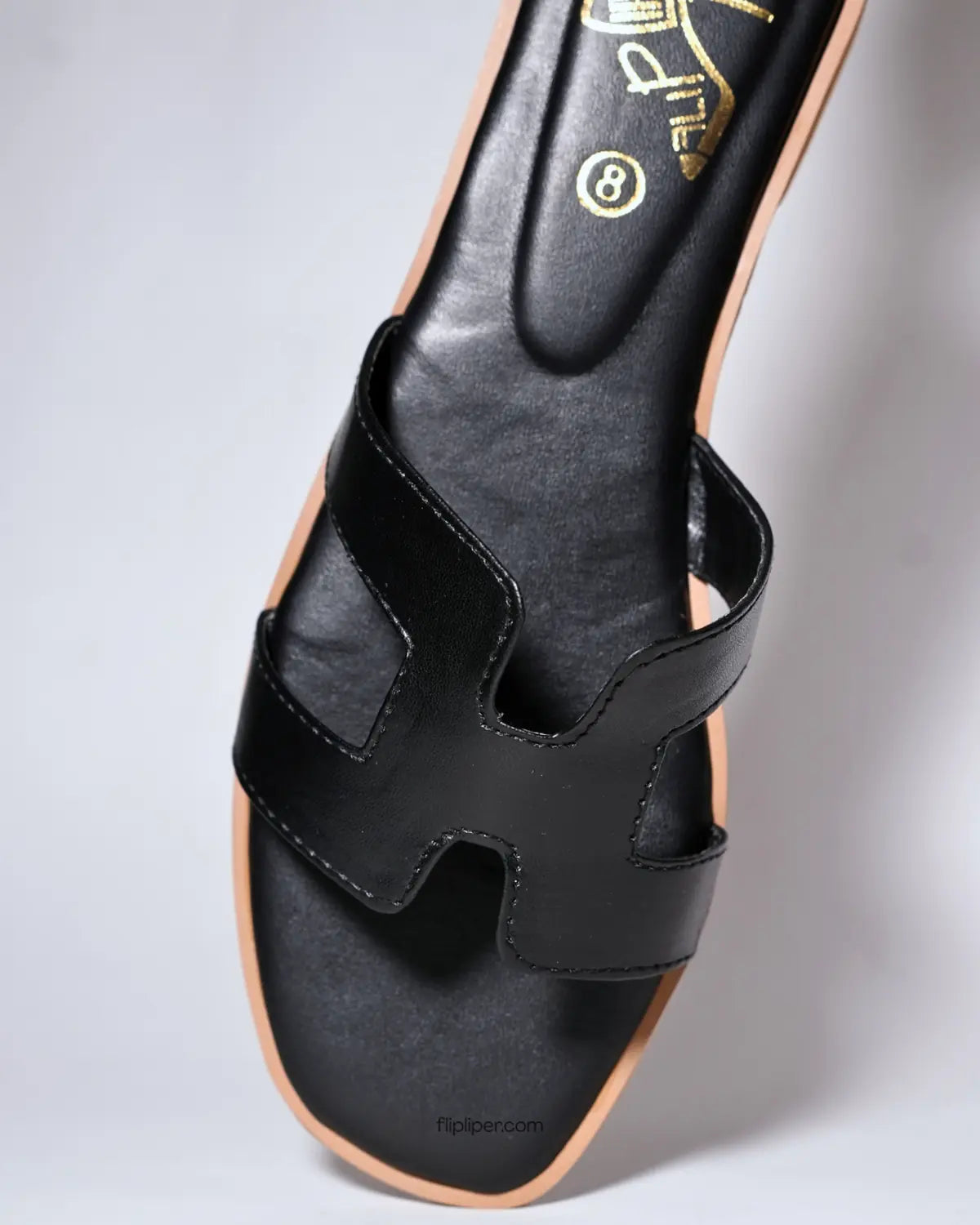 Black slip-on sandals with tan wooden soles displayed on a light beige background with minimal props
