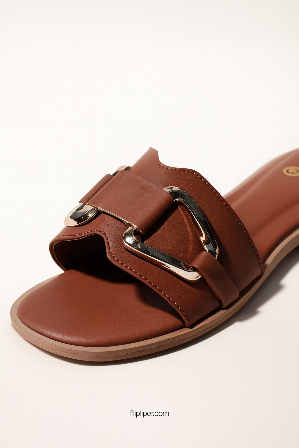 Pair of brown sandals with gold buckles displayed on a beige background
