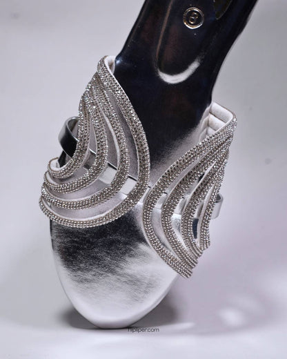 Person wearing silver embellished sandals while standing on a tiled floor
