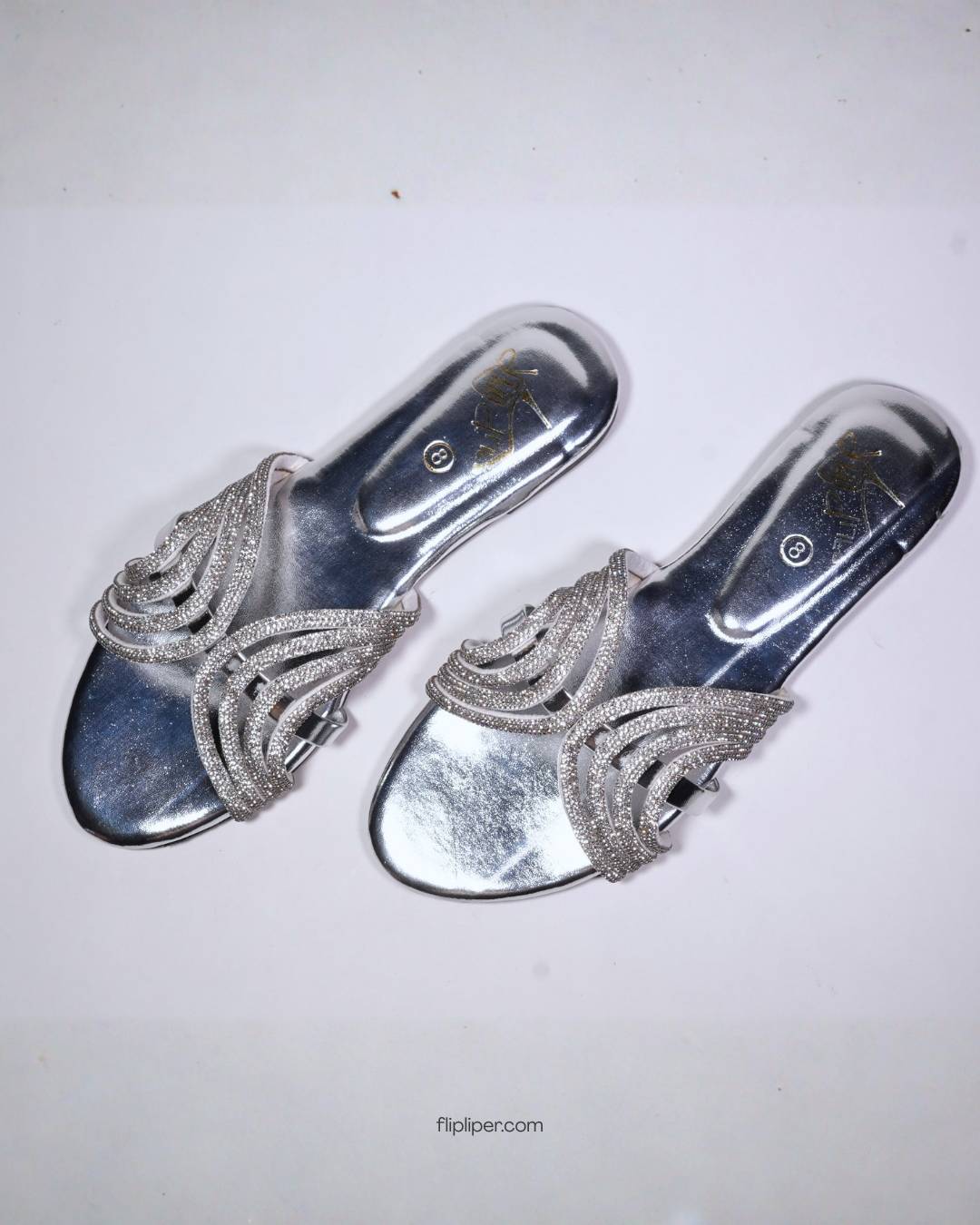 Person wearing silver embellished sandals while standing on a tiled floor
