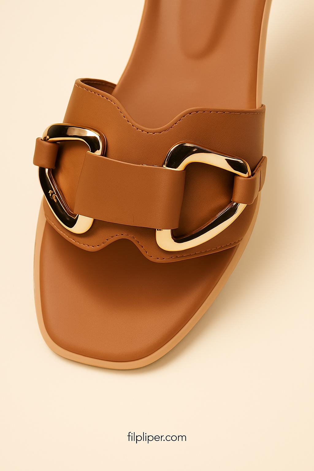 Pair of brown sandals with gold buckles displayed on a beige background
