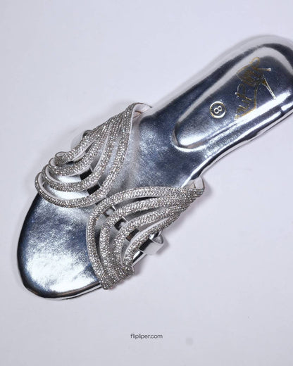 Person wearing silver embellished sandals while standing on a tiled floor
