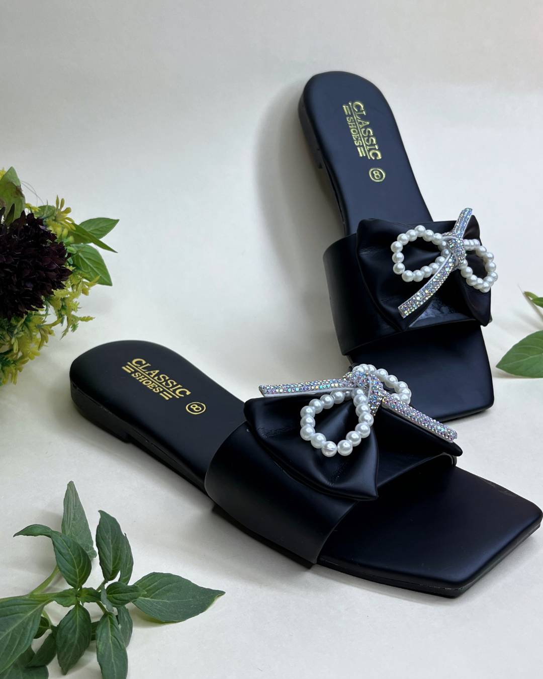 Black women luxe flats with pearl bow detailing on a light background