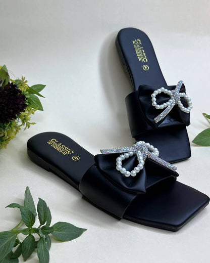 Black women luxe flats with pearl bow detailing on a light background